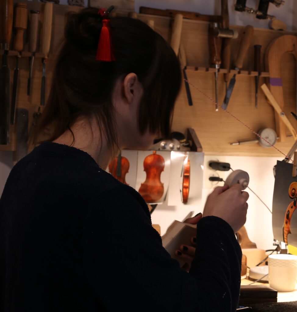 Vioolbouwer aan het werk in de werkplaats, bezig met het afstellen van een viool tussen gereedschap